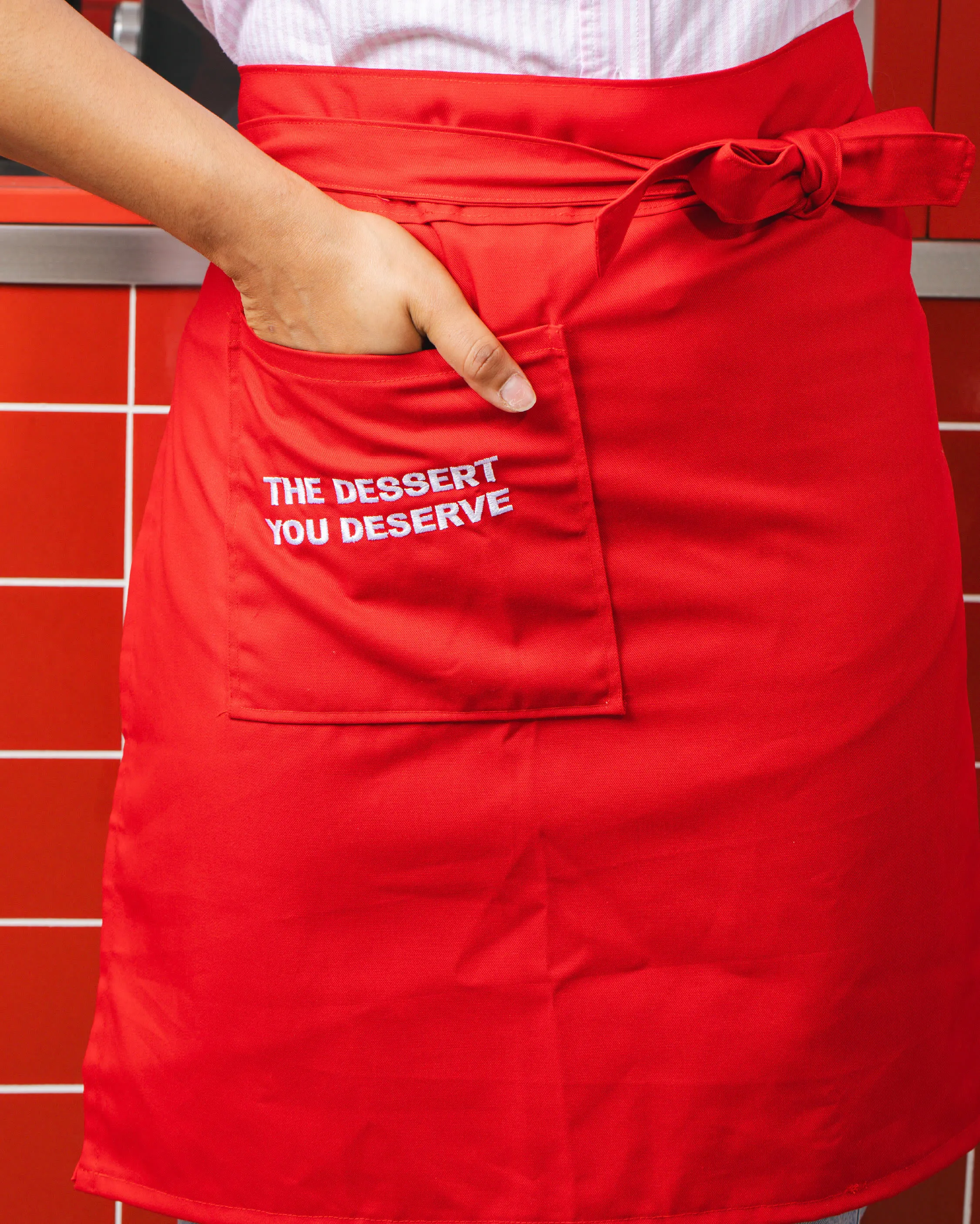 Delantal rojo con la frase «The dessert you deserve» bordada en el bolsillo