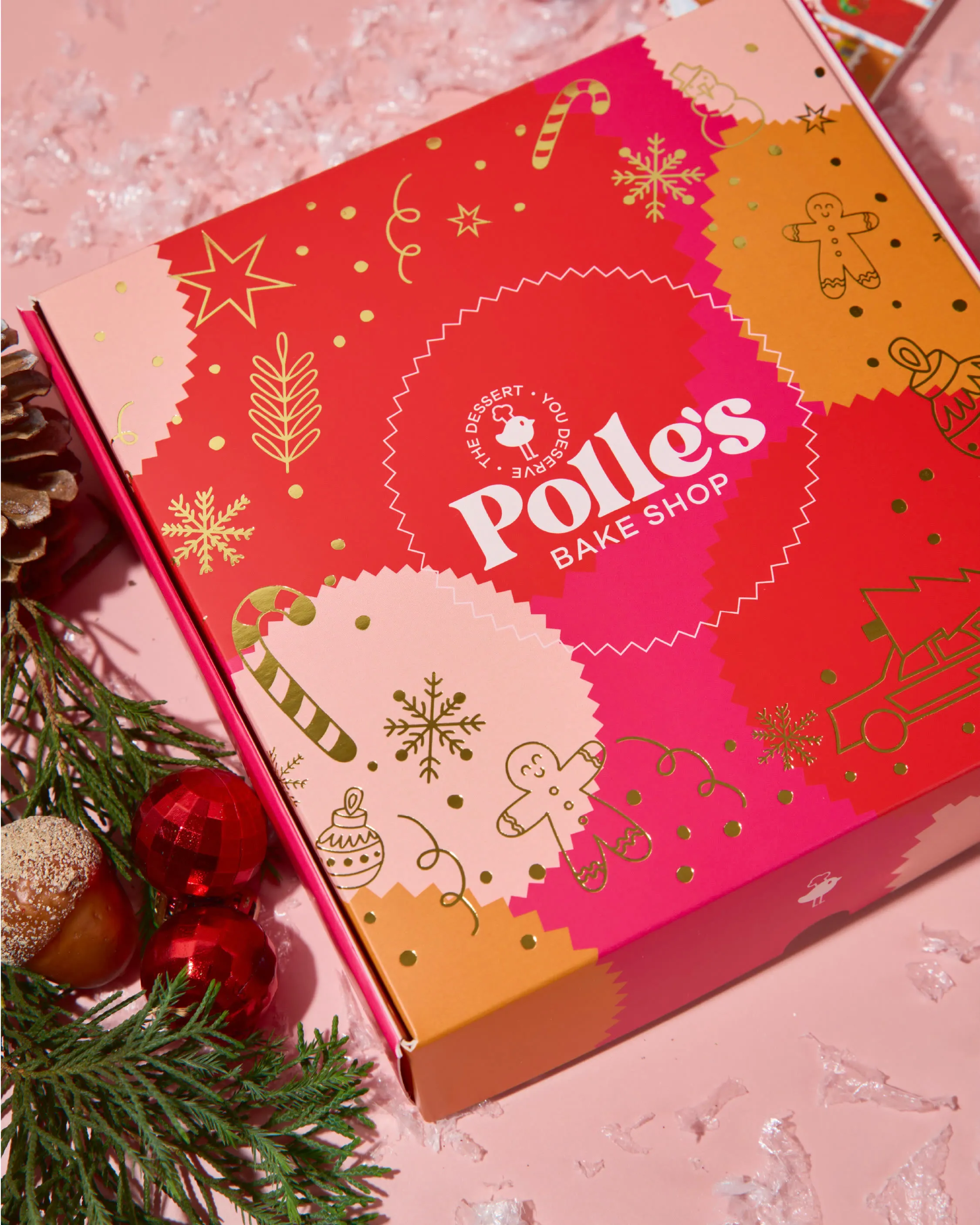 Caja navideña en rojo y rosa con ilustraciones doradas de galletas de jengibre, bastones y estrellas